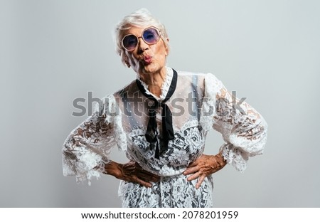 beautiful and elegant old influencer woman. Cool grandmother posing in studio wearing fashionable clothes. Happy senior lady celebrating and making party. Concept about seniority and lifestyle
