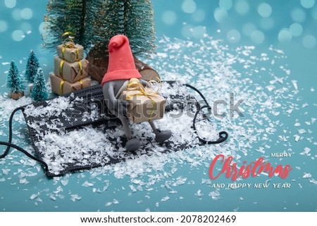 Merry Christmas greeting card with gnome sitting on snow-covered medical mask with Christmas gifts. Creative modern holiday concept