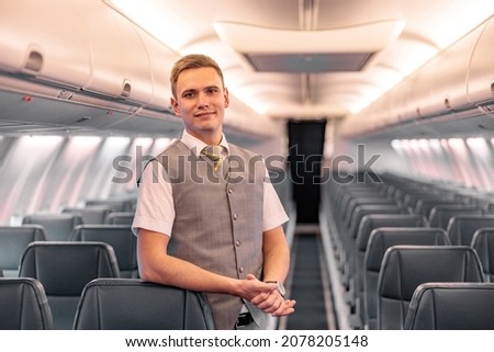 Male flight attendant standing in aircraft passenger salon Royalty-Free Stock Photo #2078205148