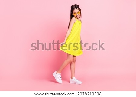 Full length photo of cute adorable school girl wear yellow dress dark eyewear smiling dancing isolated pink color background