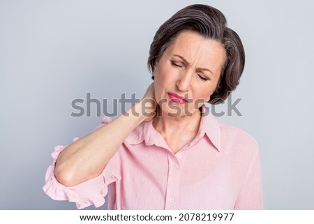 Photo of tired upset mature lady wear pink clothes arm neck having pain isolated grey color background