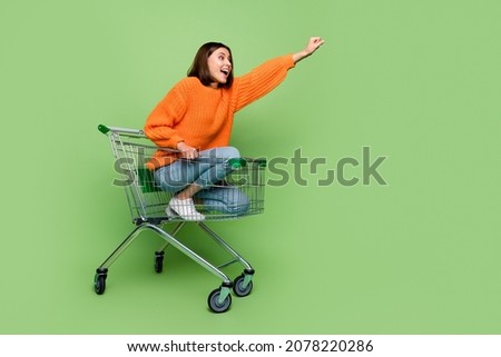 Portrait of attractive cheerful girl riding cart basket striving travel super hero isolated over bright green color background Royalty-Free Stock Photo #2078220286