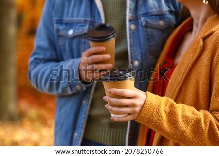 Young couple holding paper cups with drink in autumn park, closeup