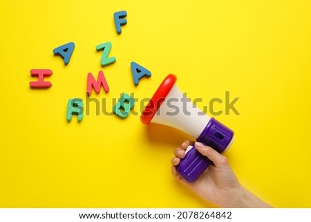 Woman with toy megaphone and letters on color background