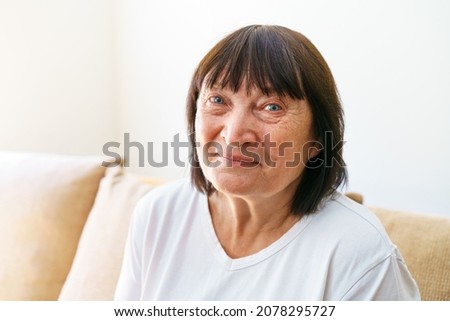 Portrait shot in head of peaceful calm middle aged woman relaxing on cozy sofa alone at home. Nice happy 60s old mature grandmother relaxing on living room couch posing for photo.