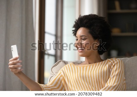 Happy young African American woman speaking on video call on smartphone, enjoying online talk, taking selfie, recording message, laughing, smiling, looking at screen, mobile phone webcam, feeling joy