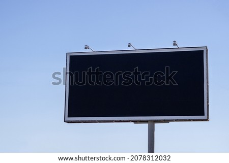 Large outdoor city black empty billboard on the blue sky.