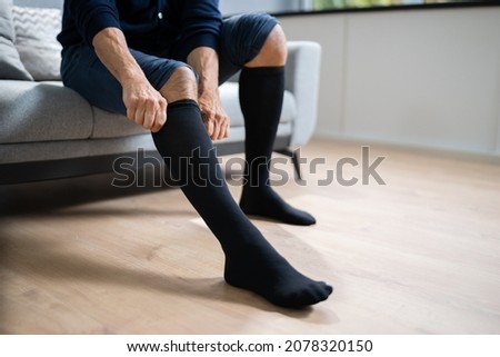 Man Putting On Medical Compression Stockings On Legs Royalty-Free Stock Photo #2078320150