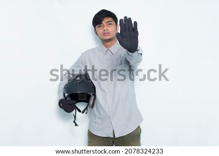 handsome asian man with a motorcycle helmet open hand doing stop sign with serious expression defense gesture isolated on white background
