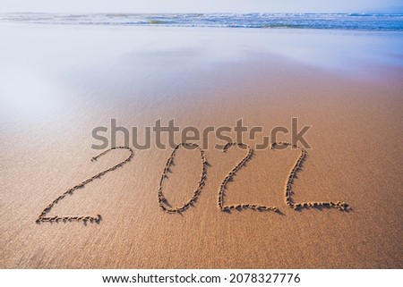 2022 hand written sign on sandy beach. Abstract seascape in golden and blue colors, copy space. Happy New Year 2022 concept