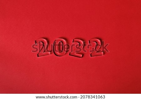 Photo of numbers 2022 made of volumetric transparent acrylic glass on a red background. Selective focusing.