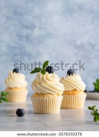Beautiful lemon vanilla cupcakes with cream cheese frosting decorated with fresh blueberries and green leaves. Delicious homemade dessert. Festive bakery. Blue background. Copy space. Close up food. Royalty-Free Stock Photo #2078350378