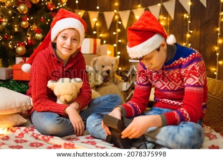 Portrait of a boy and a girl in New Year decoration. They play and take pictures. Festive lights, gifts and a Christmas tree decorated with toys.