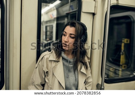 A girl in a beige trench coat rides in a subway car.
