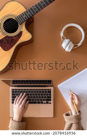 Musical background with acoustic guitar, laptop and female hands, top view.