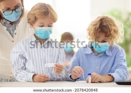 Covid-19 test in school. Rapid coronavirus antigen testing for students in classroom. Kid doing swab test kit in class. Teacher in face mask checking health exam results. Safe education in pandemic.