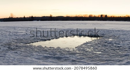 FROZEN WATER LAKE WITH CUT HOLE AT WINTER TIME, COLD OUTDOOR BACKGROUND AT THE DUSK WHILE SUNSET