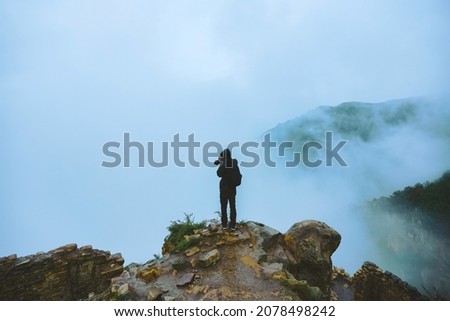 A guy hiker stands at a cliff high in the mountains and photographs the fog