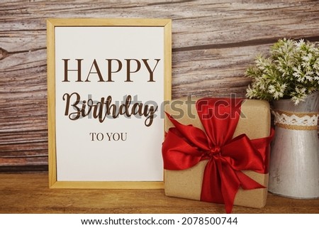 Blackboard with the text HAPPY BIRTHDAY TO YOU with gift box and red ribbon on wooden background