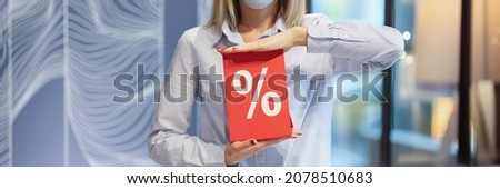 Woman in protective medical mask holding red sign with discount percentages in store. Black friday promotions and discounts concept