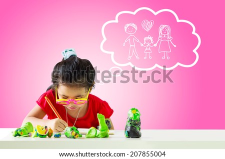 Little girl with a pencil thinking about family and writing something on table.White cloud at the top of the photo