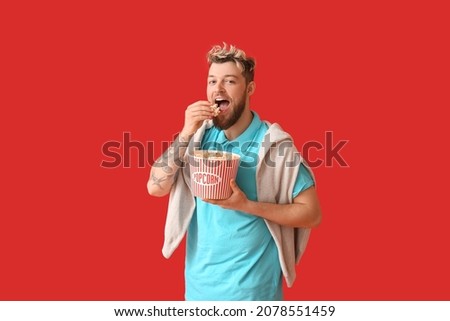 Smiling young guy eating popcorn on color background