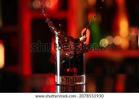 Glass of Cuba Libre cocktail with splash on table against blurred background