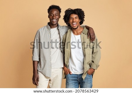 Male Friendship Concept. Portrait Of Two Happy Black Guys Embracing And Smiling At Camera, Millennial African American Mates Having Fun Together While Posing Over Beige Studio Background, Free Space