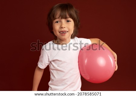 Studio image of charismatic photogenic kid of 7 years old carrying pink inflatable balloon in hand, looking happy, cheerful and excited playing with new toy, after birthday party. Carefree childhood