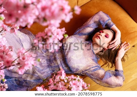 Fashion photo of beautiful young woman in beautiful dress with flowers posing lying on the couch. Fashion photo selective focus