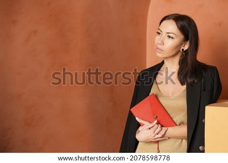 Close-up view of woman wearing black jacket and holding book with an empty red cover. Free space for your book reading concept background layout. Pensive caucasian brunette