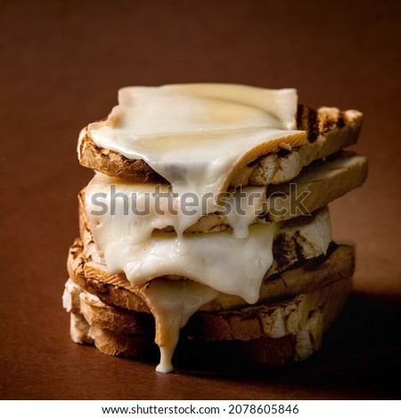 Stockpile of homemade toasted melted cheese pressed sandwiches over dark brown background. Square image