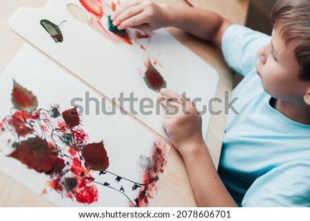 Cute child sitting at desk and making picture from dry birch leaves. Autumn activities for children