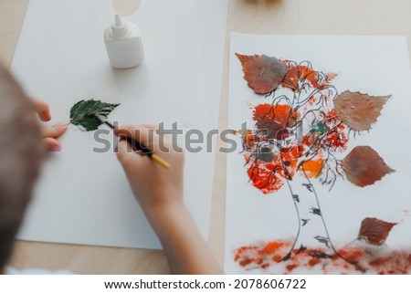 Cute child sitting at desk and making picture from dry birch leaves. Autumn activities for children Royalty-Free Stock Photo #2078606722