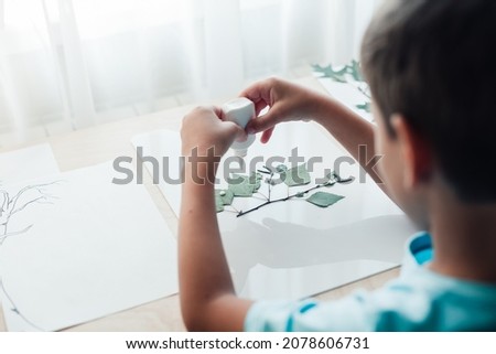 Close up of child sitting by desk and making picture from dry birch leaves. Autumn activities for children