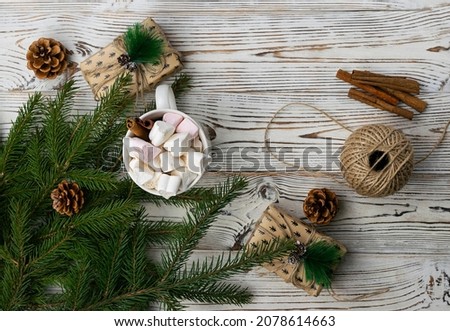 Fragrant cocoa with marshmallow and cinnamon in a white mug on a light wooden table. Fir branches with cones and balls in the background. Top view, space for text