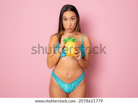 Beautiful smiling woman in bikini drinking juice isolated over pink background.