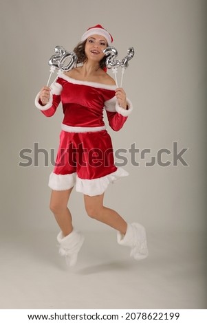 a beautiful girl in a Santa Claus hat a snow maiden costume holds the numbers 2022 in her hands jumps