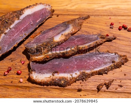 Sliced smoked gammon on a wooden table with addition of fresh herbs and aromatic spices.