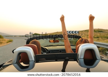 Back view of two excited women driving a convertible car in the road on summer vacation Royalty-Free Stock Photo #2078652016