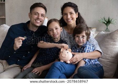30s couple and little kids sit on sofa with piggy bank smile look at camera, save money for future, children education, investment for own house manage family budget, make savings for tomorrow concept Royalty-Free Stock Photo #2078658967