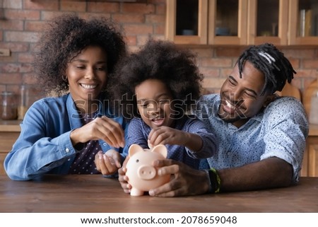 Caring young African American couple parents teaching small biracial kid daughter saving money, planning future purchases together, putting coins in small piggybank, financial education for children. Royalty-Free Stock Photo #2078659048