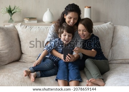 Mom and kids look at cell phone screen laughing watch funny video, play cool amusing online game, having pleasant conversation with family through videocall application, modern tech usage, fun concept Royalty-Free Stock Photo #2078659144