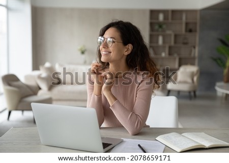 Smiling dreamy confident businesswoman in glasses looking to aside, sitting at work desk with laptop, happy pensive woman student freelancer visualizing good future, dreaming of new job opportunities