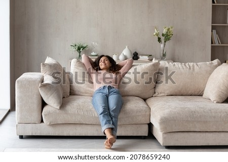 Smiling barefoot woman resting on comfortable couch at home alone, happy beautiful young female with closed eyes stretching, daydreaming or taking day nap, enjoying leisure time, no stress concept Royalty-Free Stock Photo #2078659240