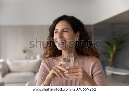 Head shot smiling dreamy woman holding glass of pure clean mineral water looking in distance visualizing, excited positive beautiful young female enjoying healthy lifestyle habit, refreshment concept Royalty-Free Stock Photo #2078659252