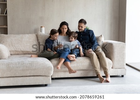 Married couple and preschool son and daughter sit on sofa reading fascinating fairy tale interesting book spend weekend enjoy favourite hobby in living room. Children development and growth concept Royalty-Free Stock Photo #2078659261