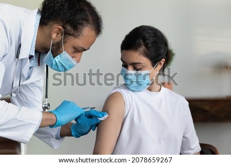 African American man doctor wearing protective medical mask and gloves injecting vaccine to young Indian woman patient in hospital, holding syringe, vaccination and healthcare, coronavirus concept Royalty-Free Stock Photo #2078659267