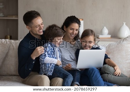 Hispanic couple and kids watching movie on laptop relaxing on sofa at modern living room. Family weekend leisure, educational online content for children, e-commerce and purchasing on internet concept
