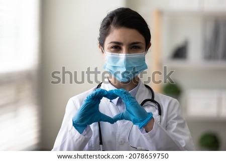 Head shot portrait happy Indian woman doctor in protective medical mask and gloves showing heart gesture, smiling young female physician practitioner looking at camera, expressing support and care Royalty-Free Stock Photo #2078659750